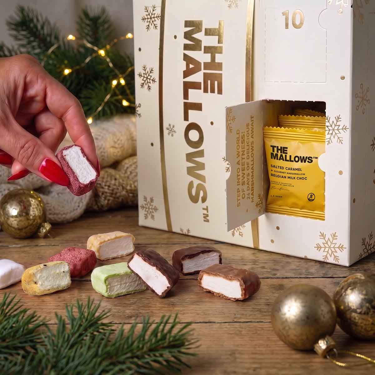 The Mallows julekalender i hvid bokd med guld hvor en hånd viser indholdet